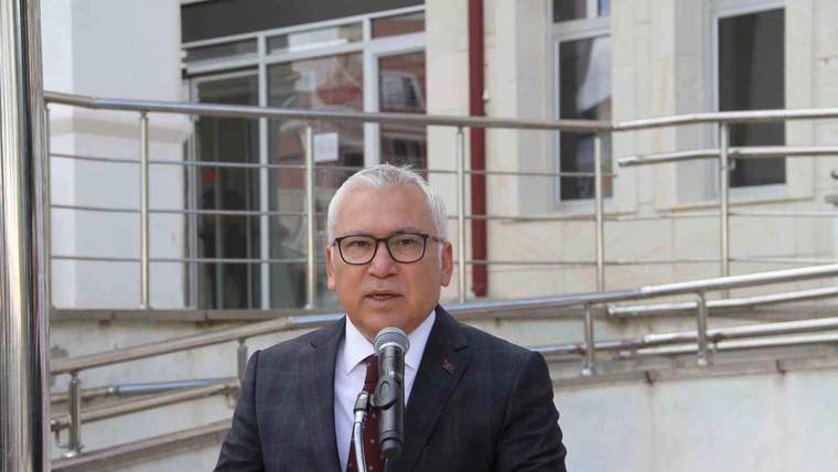 Bina girişinde kürsü arkasında duran bir kişi, mikrofonla konuşurken elindeki metne bakıyor.