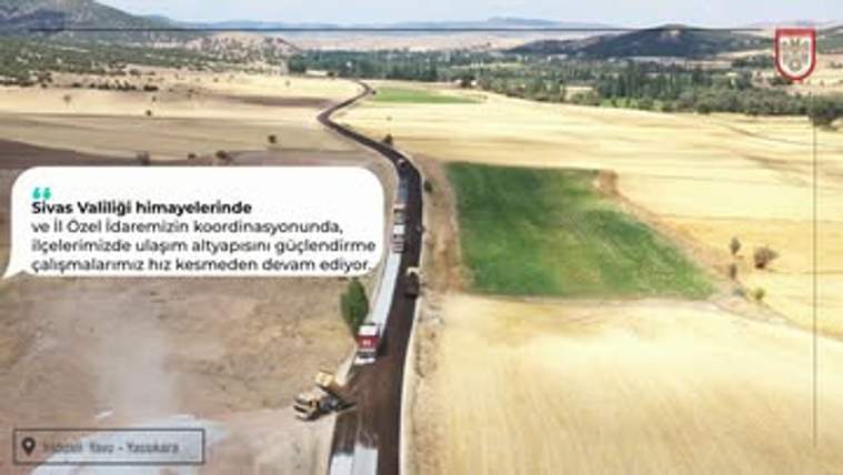 Tarlalar arasından uzanan yolda asfalt serimi yapan iş makineleri ve ilerleyen araçlar görülüyor.