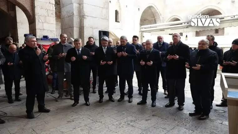 Bir grup insan, kapalı bir alanda ellerini açarak dua ediyor.
