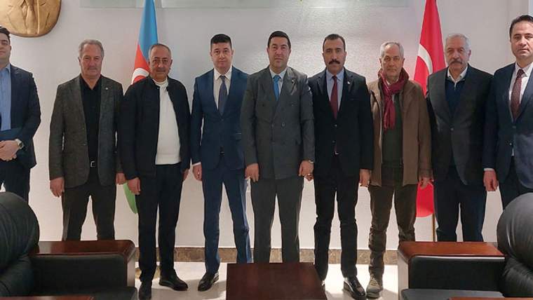 İç mekânda yedi erkek yan yana duruyor; arkalarında Azerbaycan ve Türkiye bayrakları görülüyor.