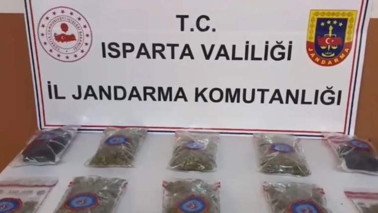 Üzerinde Isparta Valiliği ve İl Jandarma Komutanlığı yazan panonun önünde, poşetler içinde bitkisel maddeler bulunuyor.