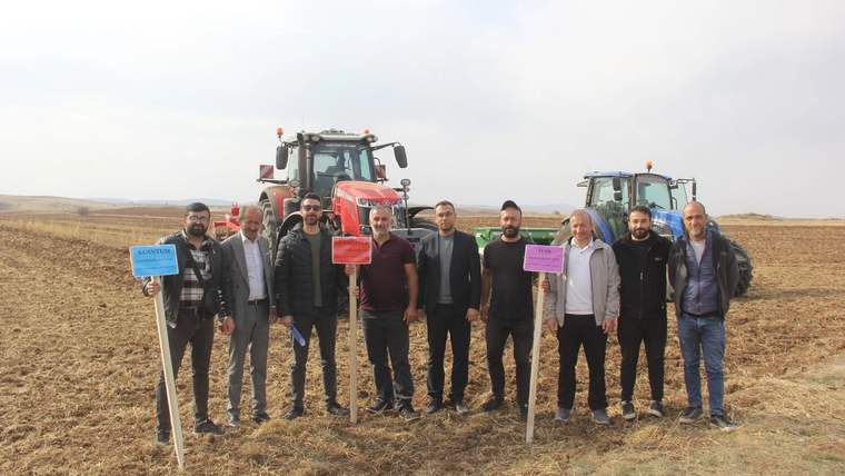 Tarla üzerinde tohum tanıtımı için bekleyen grup, arka planda traktörler var.
