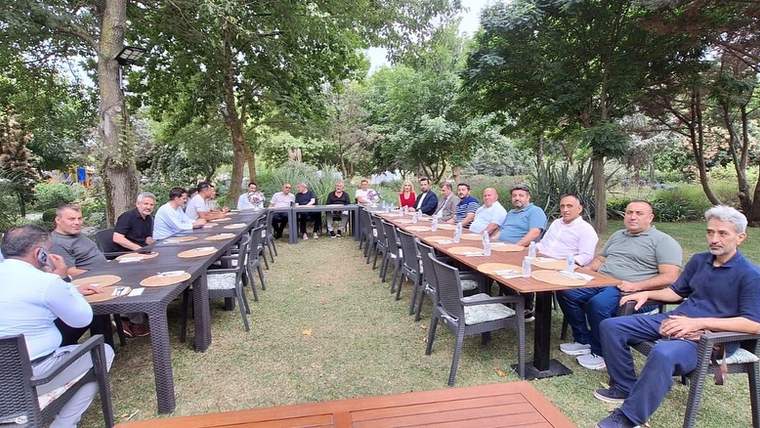 Bir bahçede uzun bir masa etrafında oturan kalabalık bir grup insan.