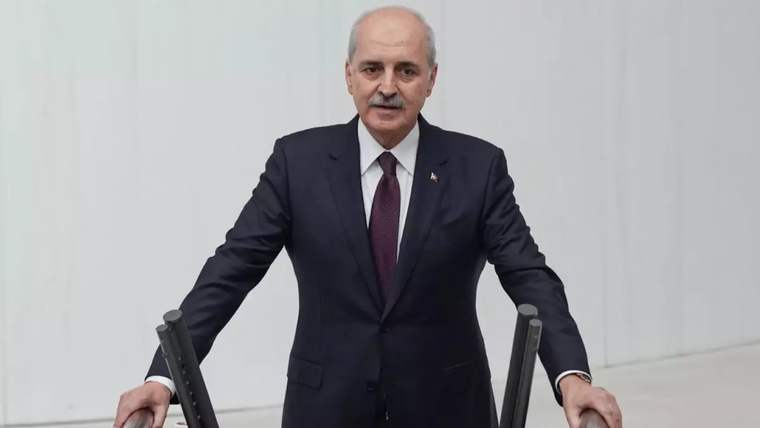 Kürsüde konuşan bıyıklı bir kişi, iki mikrofonun arasında ellerini kürsüye dayamış duruyor.