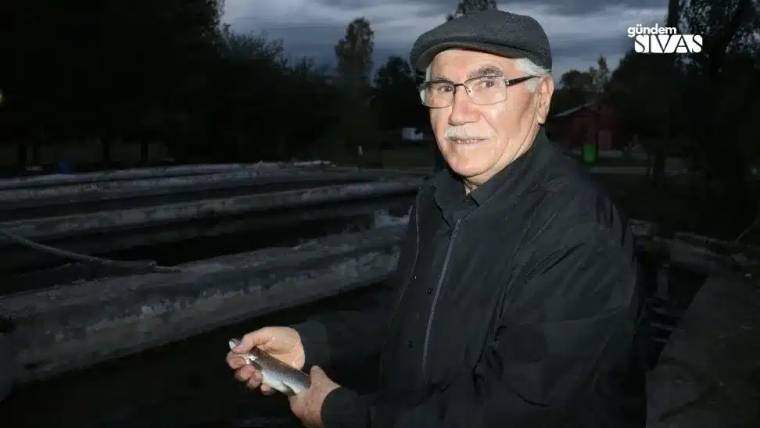 Bir kişi, elinde alabalık tutarak alabalık tesisinin yanında duruyor.