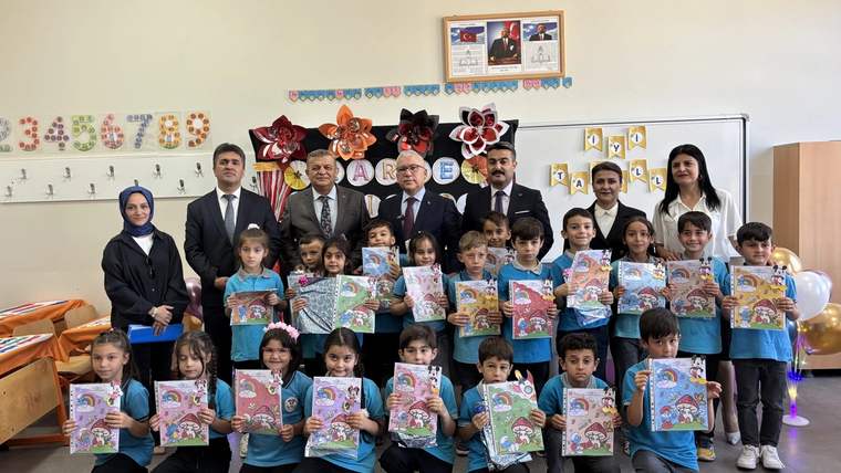 Sınıfta bir grup çocuk, ellerinde renkli belgelerle yetişkinlerin önünde yan yana duruyor.