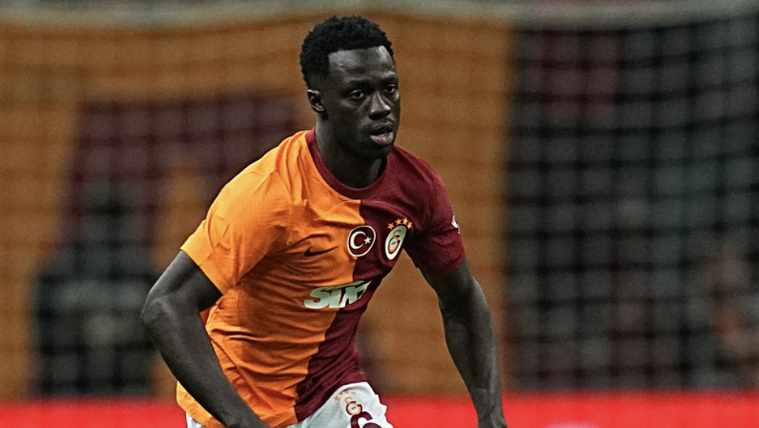 Galatasaray forması giymiş bir futbolcu, sahada koşuyor.