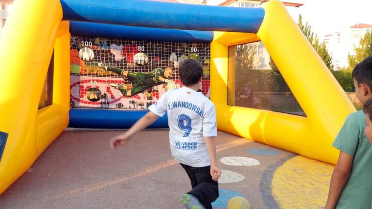 Şişme futbol oyun alanında iki çocuk, fileli kaleye doğru top sürerken görülüyor.