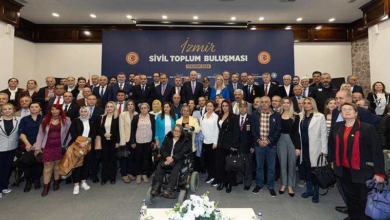 Toplantı salonunda, arkasında “İzmir Sivil Toplum Buluşması” yazılı pankart bulunan kalabalık grup poz veriyor.