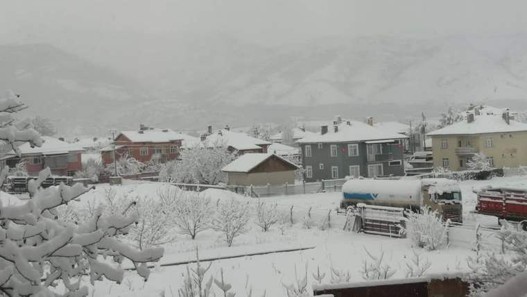 Karla kaplı bir yerleşimde evler, ağaçlar ve beyaz bir tankerin çevresini örten yoğun kar görülüyor.