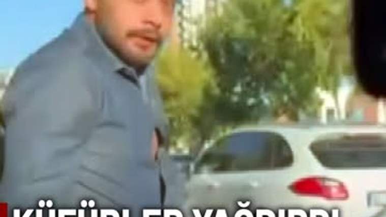 Sokakta bir kişi, park halindeki beyaz otomobilin yanında duruyor; görüntünün alt kısmında yazı bulunuyor.
