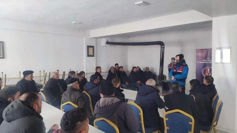 Kapalı salonda oturan kalabalığa, mavi-kırmızı yelekli bir kişi ayakta sunum yapıyor.