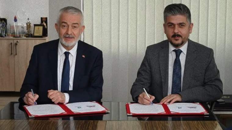 Masa başında oturan iki kişi, önlerindeki açık dosyalardaki belgeleri kalemle imzalıyor.