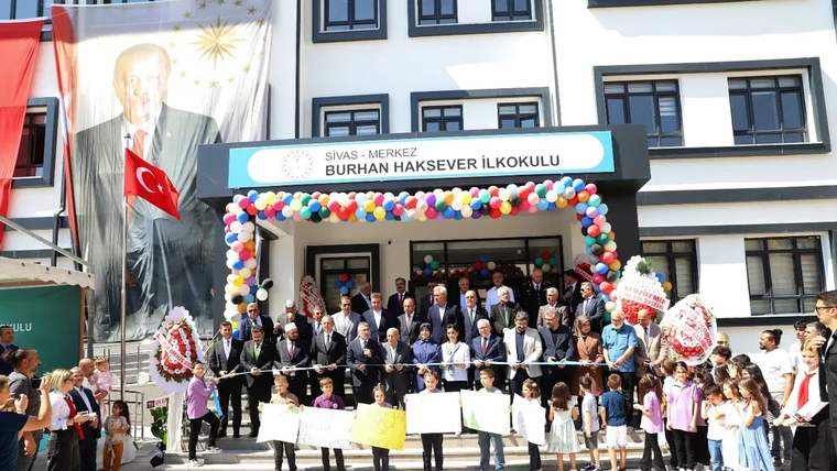 Burhan Haksever İlkokulu girişinde balonlarla süslenen kapı önünde çocuklar ve yetişkinler kurdele tutuyor.