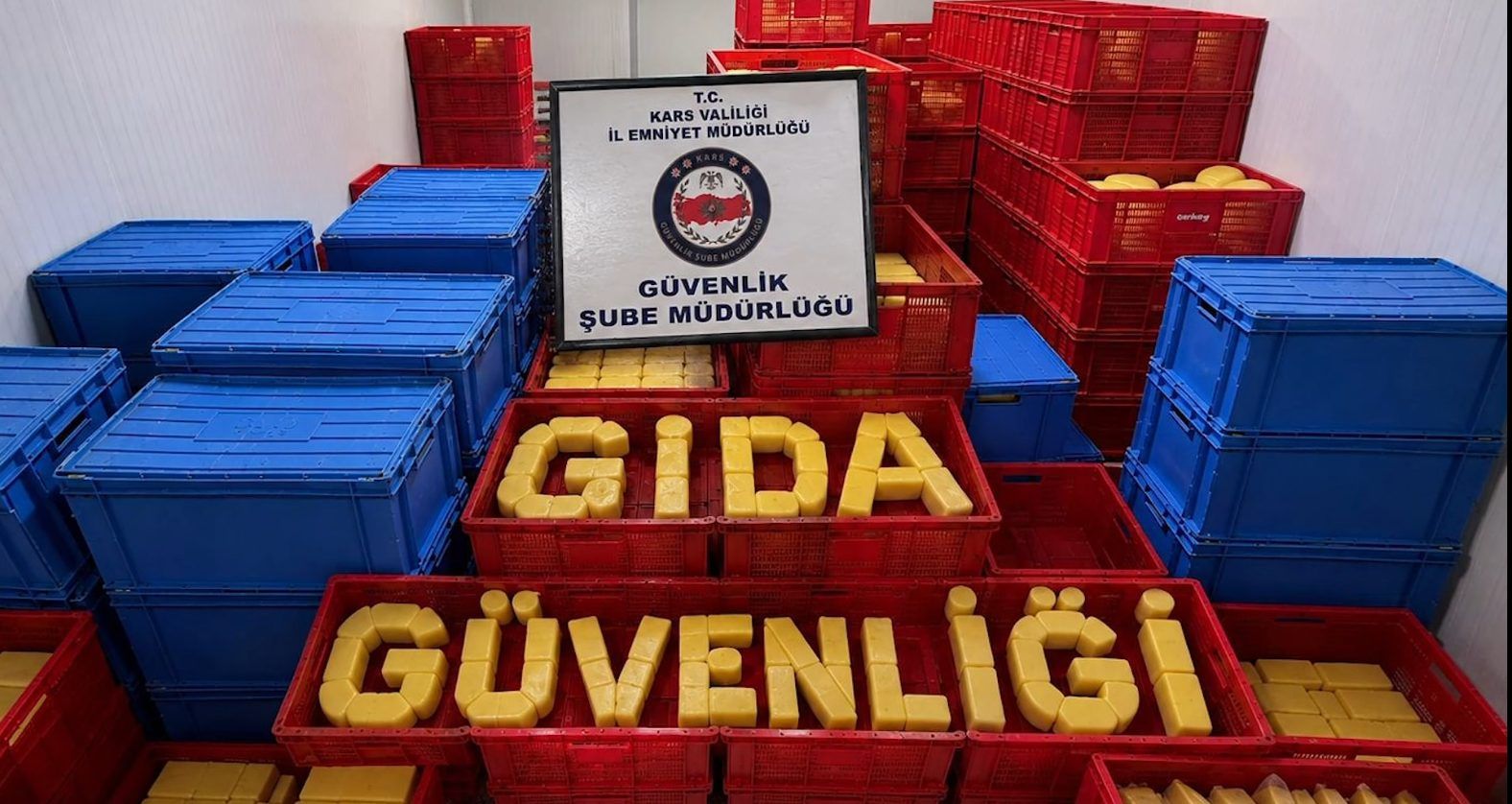 Mavi ve kırmızı kasalar arasında “GIDA GÜVENLİĞİ” yazısı ile Güvenlik Şube Müdürlüğü tabelası görülüyor.