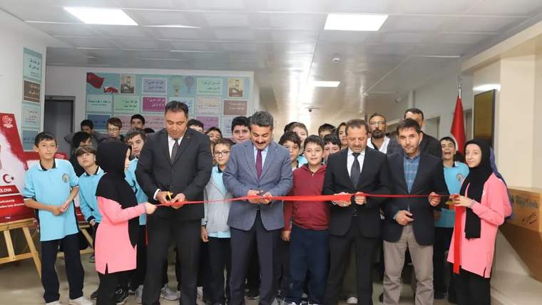 Okul koridorunda öğrenciler ve yetişkinler, kırmızı kurdeleyi makaslarla keserken yan yana duruyor.