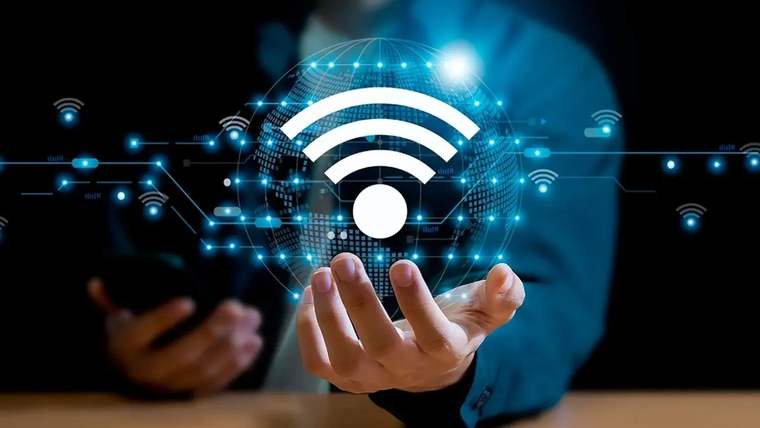 Elinde akıllı telefon tutan kişi, önünde büyük Wi-Fi simgesi bulunan ışıklı dijital küreyi gösteriyor.