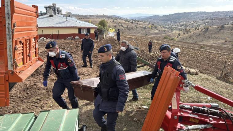 Jandarma üniformalı görevliler, kırsal arazide kahverengi bir taşıma sedyesini taşırken görülüyor.
