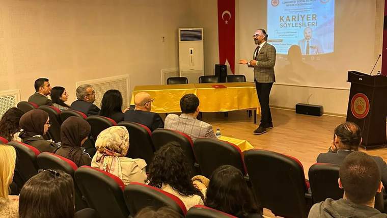 Kürsüde konuşan bir kişi, dinleyicilere kariyer sohbetleri hakkında bilgi veriyor.