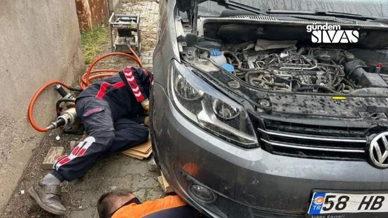 Kaputu açık otomobilin yanında iki kişi yerde çalışıyor; motor bölümü ve ekipmanlar görülüyor.