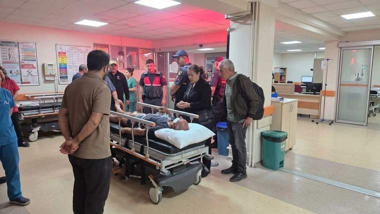 Hastane koridorunda, sedyede yatan bir kişinin çevresinde sağlık çalışanları ve birkaç kişi duruyor.