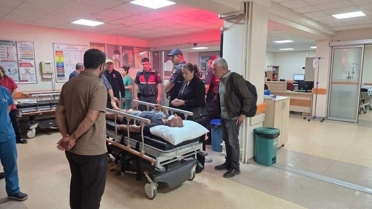 Hastane koridorunda, sedyede yatan bir kişinin çevresinde sağlık çalışanları ve birkaç kişi duruyor.