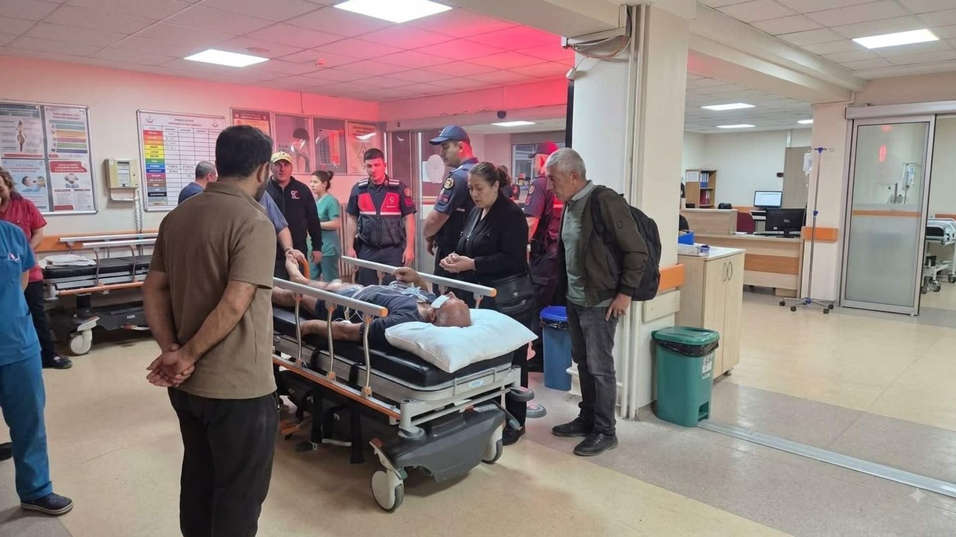 Hastane koridorunda, sedyede yatan bir kişinin çevresinde sağlık çalışanları ve birkaç kişi duruyor.