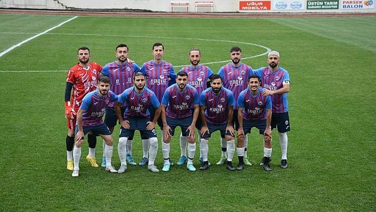 Futbol takımı, stadyumda poz veriyor; kaleci önde, diğer oyuncular arka sırada dizilmiş.