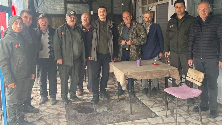 Kapalı bir alanda, çoğu montlu dokuz kişi masa ve sandalyelerin yanında yan yana duruyor.