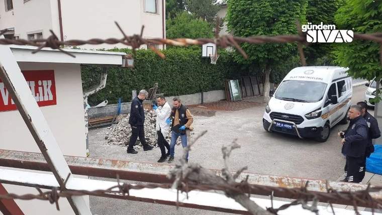 Dikenli tellerin ardından, iki üniformalı kişi bir başka kişiyi ambulansın yanından geçiriyor.