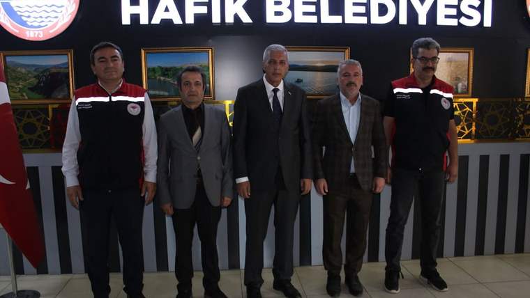 Hafik Belediyesi binasında, beş kişi bir arada duruyor; arka planda Hafik Belediyesi logosu var.