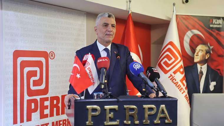 Kürsüde konuşan bir kişi, çok sayıda mikrofon ve Türk bayrakları önünde PERPA yazılı platformda duruyor.