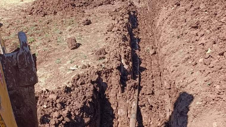 Toprak zeminde açılmış dar bir kanalda boru uzanıyor; sol kenarda iş makinesinin kepçesi görülüyor.