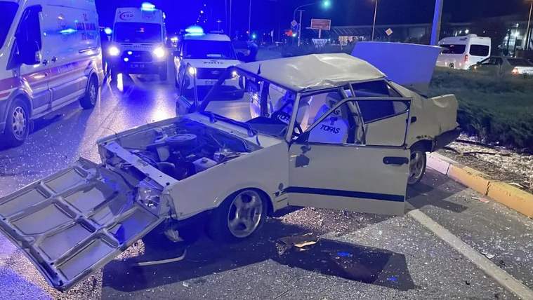 Yolda devrilmiş bir Tofaş otomobil, etrafında acil yardım araçları ve mavi ışıklar var.