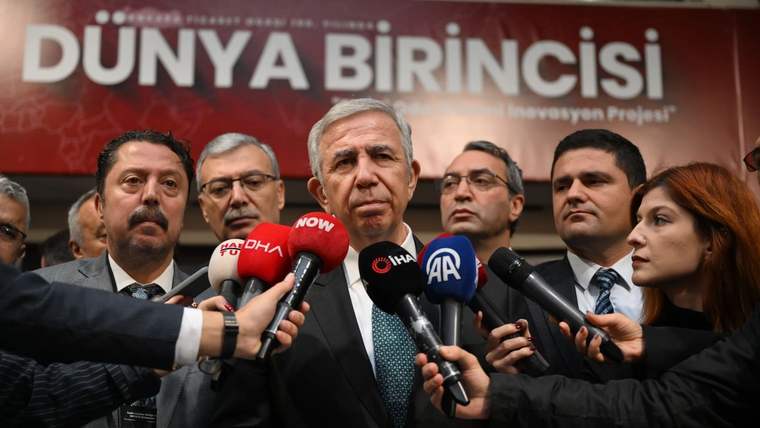 Kürsü önünde konuşan bir kişinin çevresinde çok sayıda mikrofon ve gazeteci, arkada “DÜNYA BİRİNCİSİ” yazısı var.