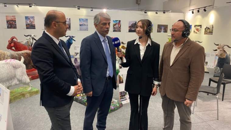 Dört kişi, bir sergi alanında mikrofonla röportaj yapıyor; arka planda çeşitli hayvan figürleri var.