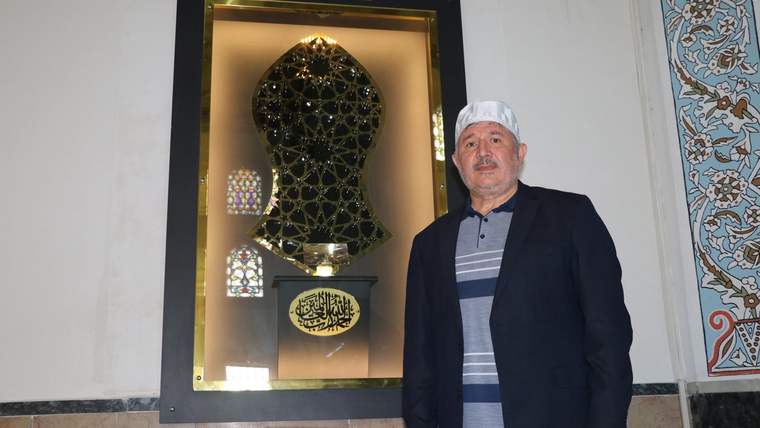 Camlı bir vitrinde “SAKAL-I ŞERİF” yazılı muhafaza, yanında duran bir erkek ve süslemeli duvar görülüyor.