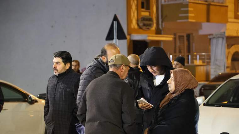 Havalimanı önünde bir grup insan, cep telefonuna bakarak sohbet ediyor.