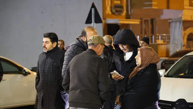 Havalimanı önünde bir grup insan, cep telefonuna bakarak sohbet ediyor.