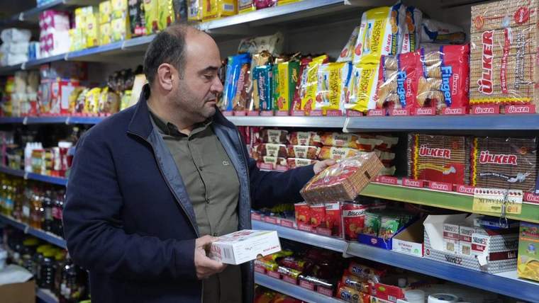 Bir markette ürünleri inceleyen bir kişi, rafta çeşitli gıda ürünleri yer alıyor.
