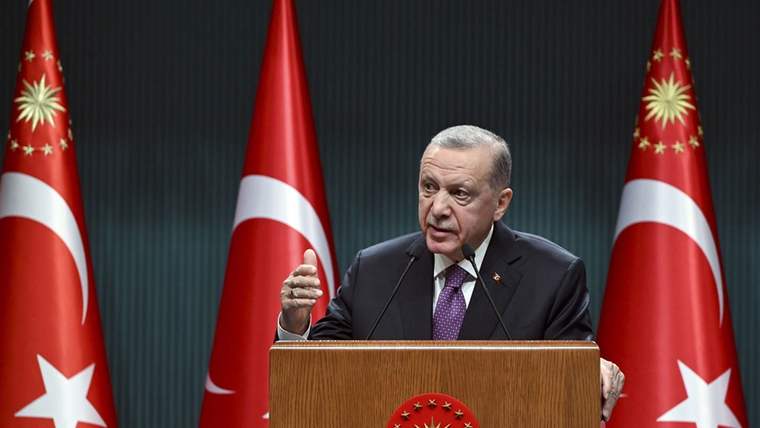 Kürsüde konuşan bir kişi, arkasında Türk bayraklarıyla birlikte açıklama yapıyor.