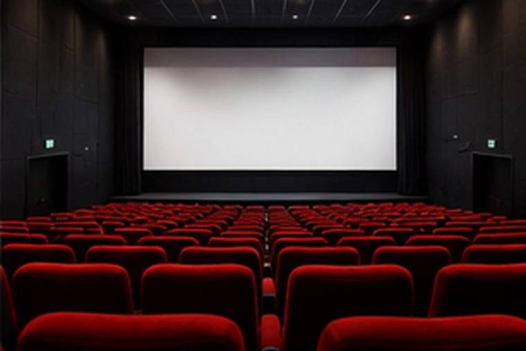 Boş bir sinema salonunda beyaz perde ve sıralar halinde kırmızı koltuklar görülüyor.