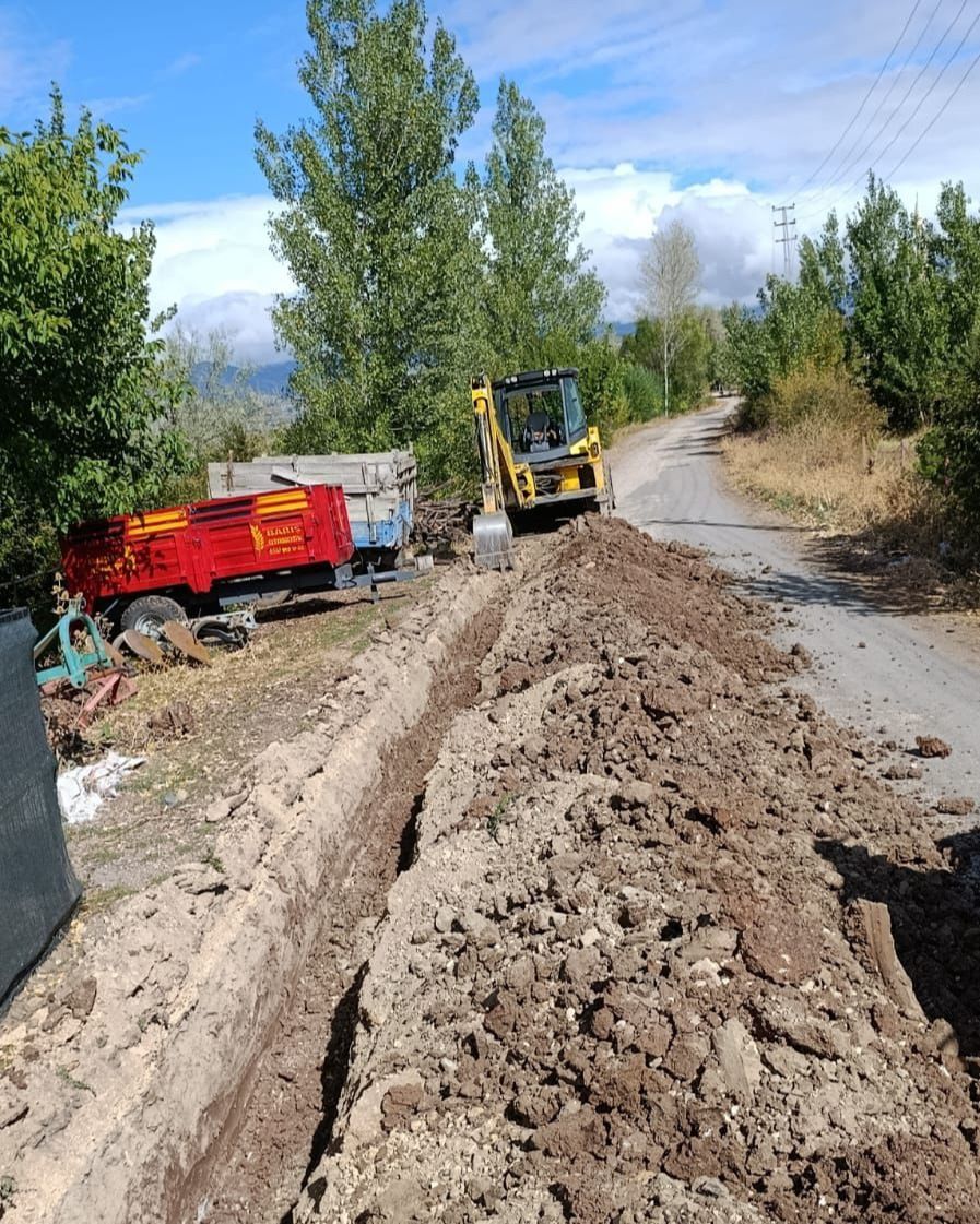 Yolda kazı çalışması yapan bir iş makinesi, etrafında toprak ve inşaat malzemeleri var.