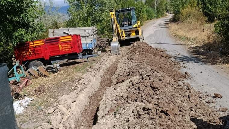 Yolda kazı çalışması yapan bir iş makinesi, etrafında toprak ve inşaat malzemeleri var.