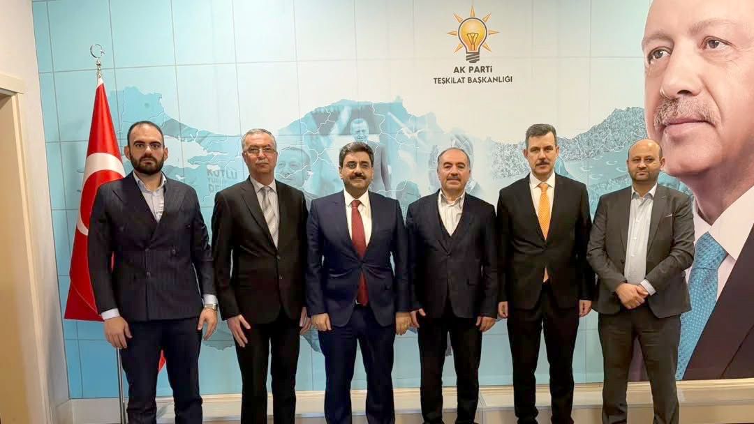AK Parti binasında, altı kişi yan yana duruyor; arka planda Türkiye haritası ve parti logosu var.