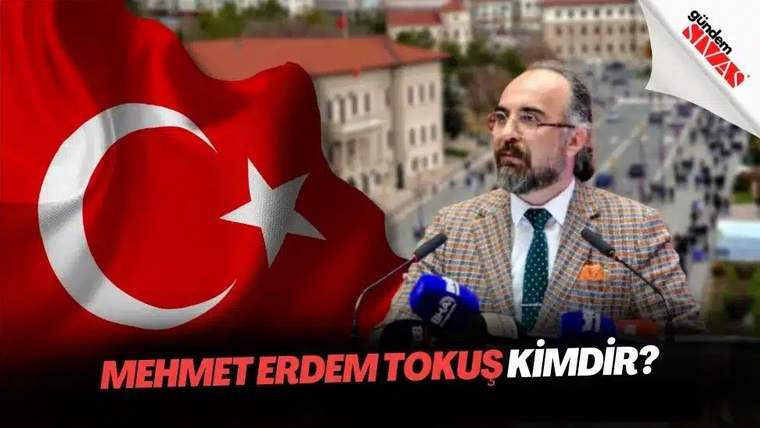 Bir kişi, arka planda Türk bayrağı ve bir bina ile birlikte konuşma yapıyor.