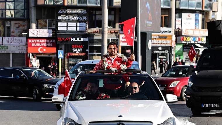 Türk bayrağı tutan bir kişi, çiçeklerle süslenmiş bir araçta oturuyor.