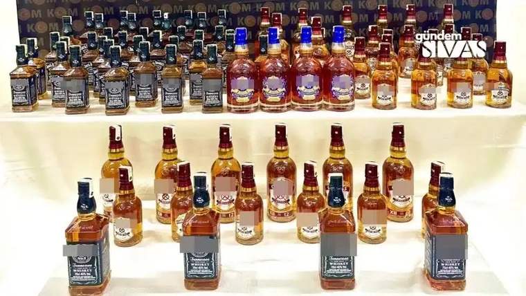 Dizili halde çeşitli markalarda sahte alkol şişeleri, arka planda kaçak tütün paketleriyle birlikte.