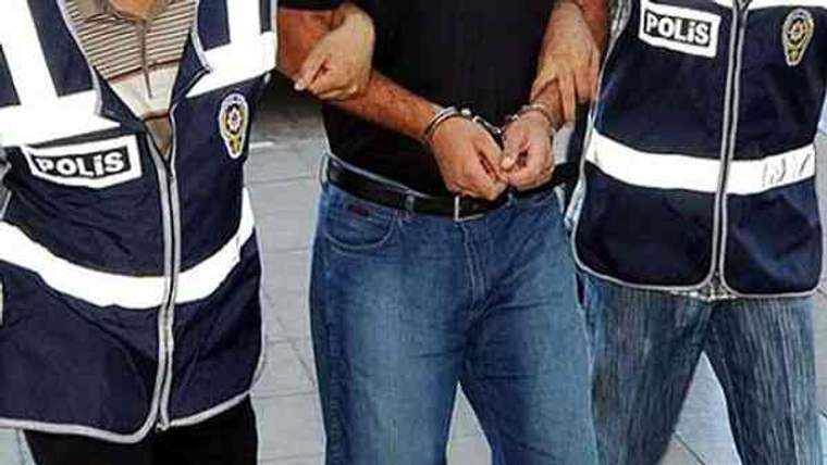 İki polis yelekli görevli, elleri kelepçeli bir erkeği kollarından tutarak yürütüyor.