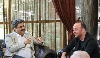 İç mekânda koltuklarda oturan iki erkek sohbet ederken biri elleriyle açıklama yapıyor.